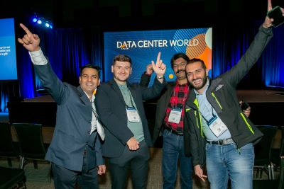 4 people standing with arms raised and smiling in front of the Data Center Live! Stage.